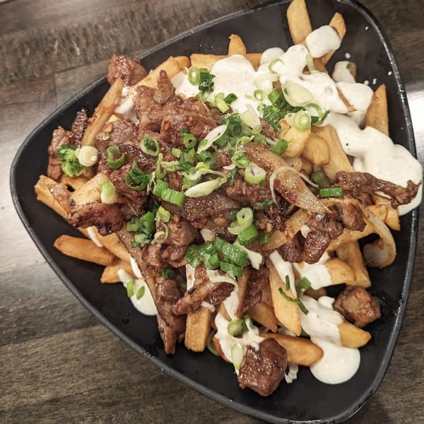 Japanese steak fries with white sauce and green onions on a black plate.