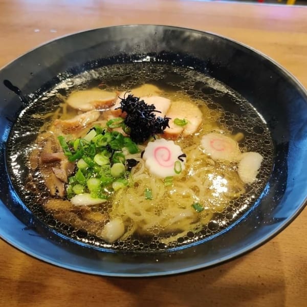 A close-up of a bowl of Senzu Noodle Bar ramen with pork, seaweed, and green onions.