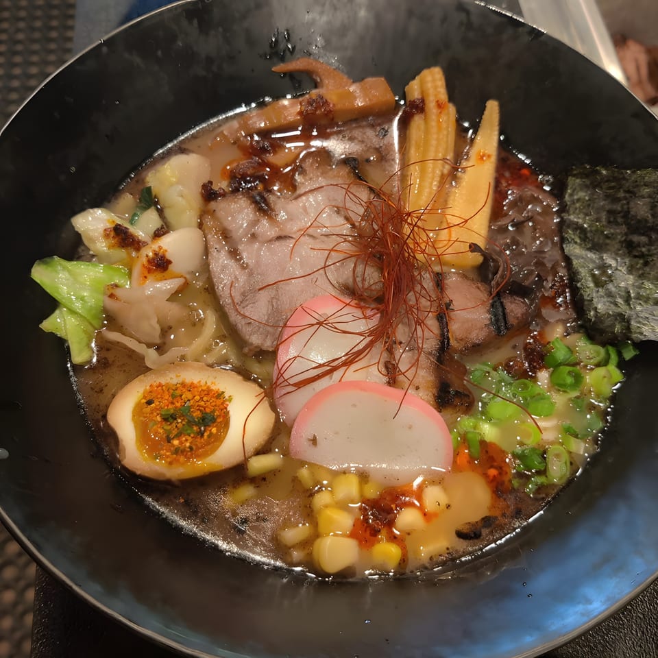 A close-up of Senzu Noodle Bar's ramen with pork, egg, baby corn, fish cake, and chili threads.